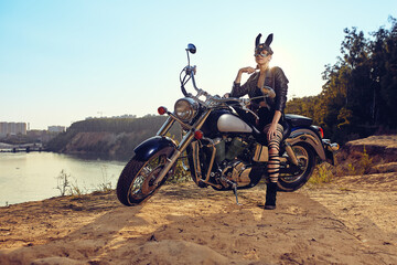 A beautiful sexy young woman in leather jackets and rabbit mask sitting on a black and chrome motorbike