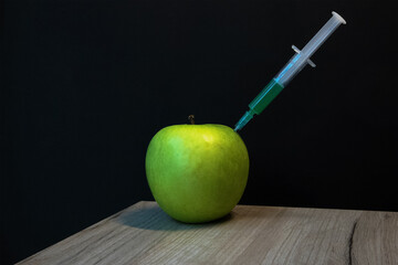 Green apple on a wooden board and syringe inside it extracting green liquid