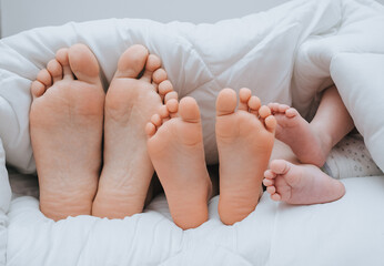 Close-up of the legs of the family of mom, daughter and little newborn son, covered with a plaid....