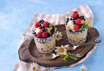 Dessert, truffle with biscuit, fresh blueberries, raspberries and custard or cream in glasses on a light background. Desserts recipes with berries, blueberries. British cuisine.