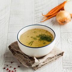 Homemade broth in a white bowl on a napkin with dill, fresh carrots and onions. concept of healthy eating. Copy space.