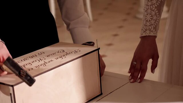 The groom nails a nail into the lid of a wooden box. Wedding ritual. Close up