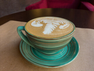 Сup of latte stands on the table. The cup stands on a saucer and both are made in the characteristic sloppy Japanese ceramic style.