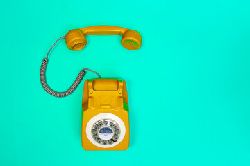 Yellow handset of a telephone on a green mint background.