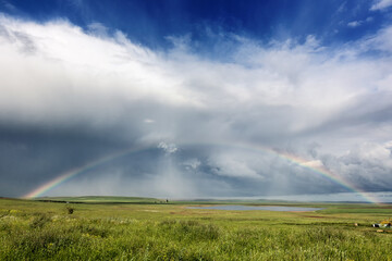 Fototapeta na wymiar Beautiful landscape after the rain. A field with a big rainbow and a beautiful rainbow.