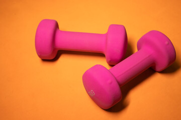 Bright pink small dumbbells on an orange background. Sport concept. High quality photo