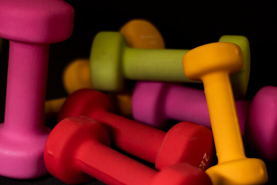 Bright pink, green, red and yellow small dumbbells on a black background. Sport concept. High quality photo