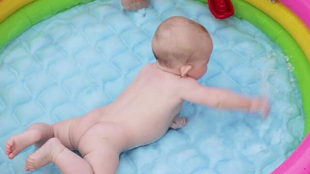 Cute little child, toddler boy, playing in small baby inflatable pool in backyard. Happy newborn splash water in the pool in summer country house. Healthy lifestyle. Happy family. Swimming in pool.