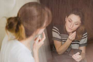 Beautiful modern caucasian woman doing make-up by herself looking at the mirror.