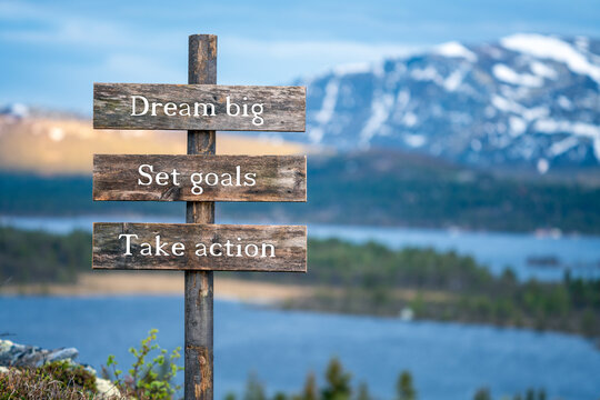 dream big set goals and take action text on wooden signpost outdoors in landscape scenery during blue hour and sunset.