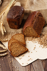 Bread in form of triangle and with sunflower seeds near spikelets of wheat lies on old weathered wooden table. Rustic bread and wheat on an old vintage planked wood table. Free text space.