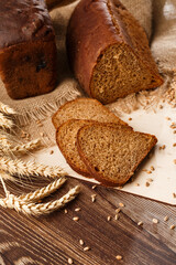 Bread in form of triangle and with sunflower seeds near spikelets of wheat lies on old weathered wooden table. Rustic bread and wheat on an old vintage planked wood table. Free text space.