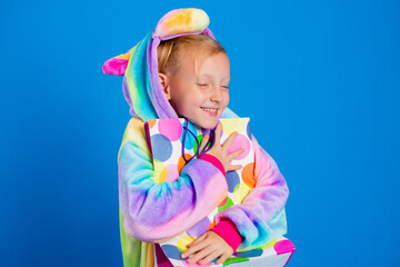 A happy little girl in a unicorn kigurumi holds a gift bag. multicolored confetti. concept of birthday, holiday, sale. Space for text