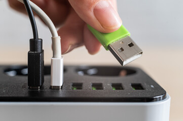 Modern convenient multi-port usb charger for devices. Close-up of a female hand plugging multi-colored cables into a power outlet. Macro.