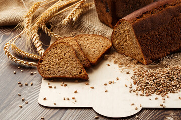 Bread in form of triangle and with sunflower seeds near spikelets of wheat lies on old weathered wooden table. Rustic bread and wheat on an old vintage planked wood table. Free text space.