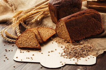 Bread in form of triangle and with sunflower seeds near spikelets of wheat lies on old weathered wooden table. Rustic bread and wheat on an old vintage planked wood table. Free text space.