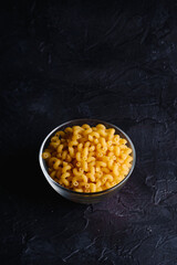 Glass bowl with cavatappi uncooked golden wheat curly pasta on textured dark black background, angle view copy space