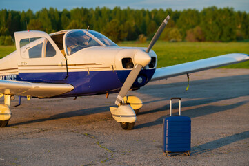 A blue suitcase and a landed small private jet. Four-seater plane with a propeller for the air...