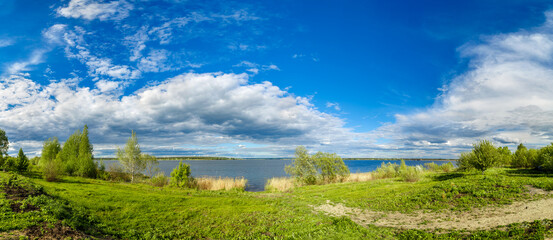 Fototapeta na wymiar Summer landscape with lake, blue sky and clouds. Nature wilderness. Countryside outdoors, relaxation, space scenic. Beautiful pond, forest, green meadow with reflection in water. Panoramic views.