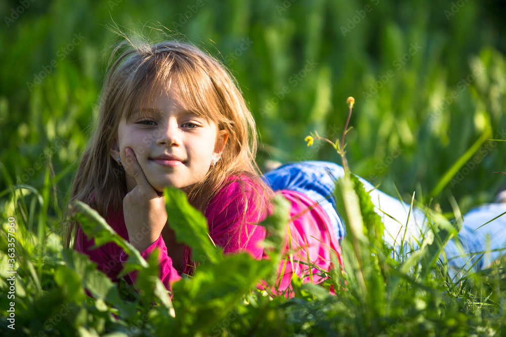 Wall mural Ten-year-old funny girl lying in the grass outdoors.