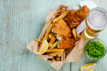 Deep fried fish and chips with lemon slices, green peas and beer