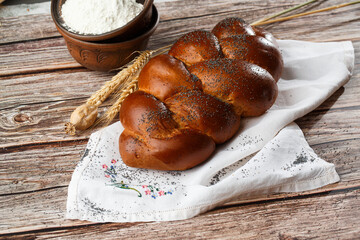 Homemade Jewish traditional challah bread on white napkin on wooden table. Homemade Decorated with poppy seeds. Jewish cuisine. Copy space for text, brand or logo. Close up and top view