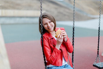 Young girl eating a burger outdoors. Girl with pleasure eats fast food on the street. Attractive girl bites a burger