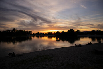 People sitting and relaxing on the shore of Jarun lake in Zagreb, observing beautiful, summer sunset