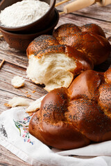 Homemade Jewish traditional challah bread on white napkin on wooden table. Homemade Decorated with poppy seeds. Jewish cuisine. Copy space for text, brand or logo. Close up and top view