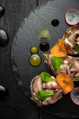 Meat bruschettas with cheese, vegetables, on a dark stone board
