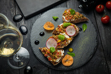vegetarian bruschettas with cheese, vegetables, on a dark stone board

