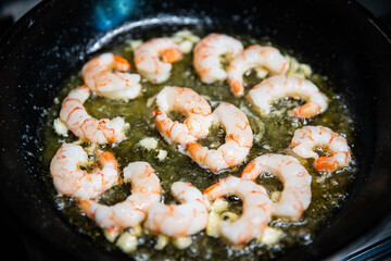 Process of frying giant red shrimps with garlic on olive oil on pan.