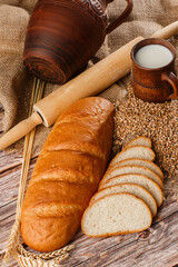 Close-up of homemade bread. Peasant loaf bread and wheat spikelets with space for text. Homemade baking. White bread with flour and milk on wooden chopping board wheat rye ears copy space.