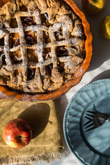 Traditional apple pie in ceramic baking form, apples and plates on white kitchen.