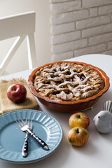 Traditional apple pie in ceramic baking form, apples and plates on white kitchen.