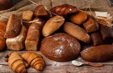 Different kinds of fresh bread as background, top view. Bakery gold rustic crusty loaves of bread and buns on wooden background. Still life captured from above. Kitchen or bakery poster design.