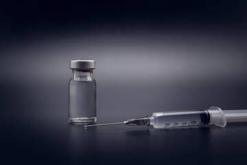 Small vaccine bottle (phial) and a medical syringe injection with a vaccine drop on its needle, isolated on black background