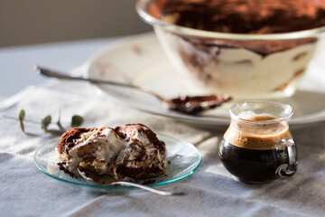 Glass bowl and plate with tiramisu dessert on white kitchen table.