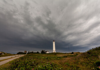 A heavy thunderstorm is catching up over the lighthouse Blåvandshukfyr at the North Sea coast in Denmark causing a dramatic dark grey sky