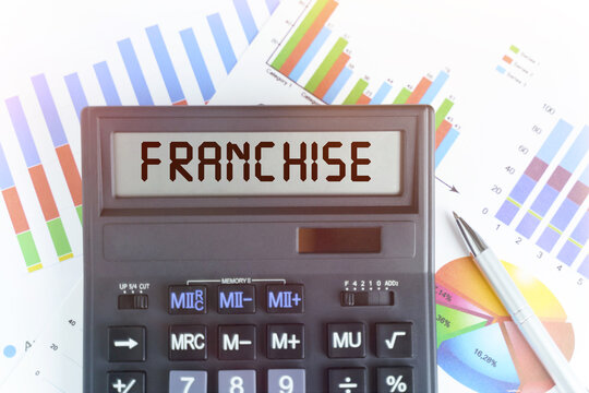 On The Table Are Financial Charts And A Calculator, On The Electronic Board Of Which Is Written The Text - FRANCHISE