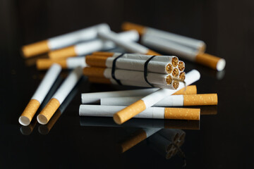 Cigarettes, in the form of sticks of dynamite, lie among the scattered cigarettes on a black reflective surface.