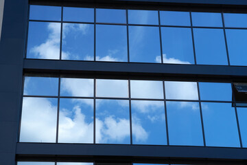 facade of a modern building on a bright Sunny day, blue sky and clouds reflecting in a glass, beautiful exterior of the new building