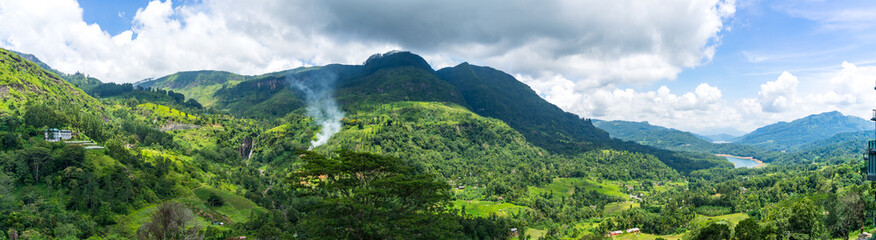 Fototapeta na wymiar Panoramic landscape of Sri Lanka. waterfall in the mountains and tea plantation. smoke behind trees.