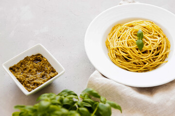 A plate with traditional Italian pasta pesto next to a gravy boat with basil sauce. Copy space