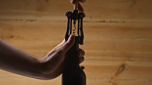 cropped view of man opening bottle with corkscrew