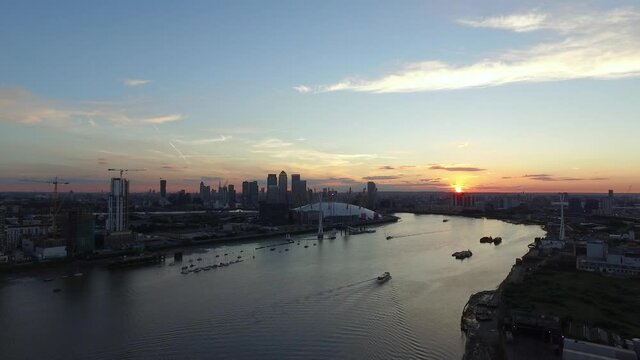 Aerial drone shot over the river Thames towards the London skyline as the sun sets in the distance
