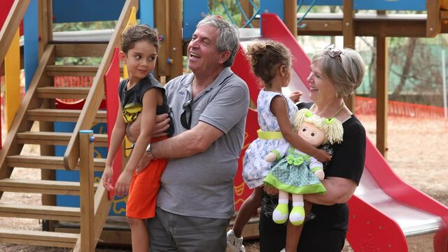 Video in 4k di due nonni bianchi che giocano con i loro nipoti di pelle scura all'interno di un parco giochi