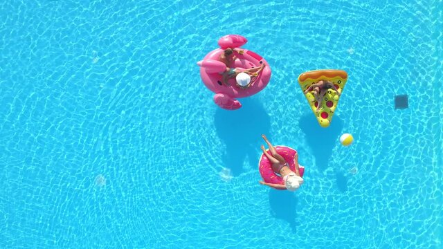SEAMLESS CINEMAGRAPH LOOP, AERIAL, TOP DOWN: Flying above a group of friends relaxing on cool floaties during a pool party. Young tourists chill out at the pool during their carefree summer vacation.
