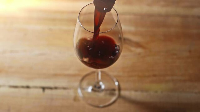 slow motion of red wine pouring in wineglass on wooden table