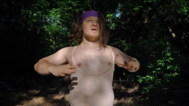Playful Fat Man with Long Hair in Funny Clothes Doing Fitness Depicting a Girl in Nature